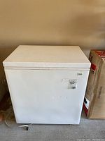 Front view of white Kenmore chest freezer with hinged lid, showing some surface marks and a label taped to the front.