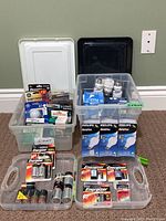 Three plastic bins shown filled with various boxes and loose light bulbs and batteries.