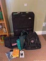 Front view of large black Samsonite suitcase and assorted bags including a Roots knapsack, Costco bag, and various reusable bags, plus luggage scale and assorted straps.