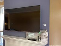 Wall-mounted Panasonic Viera 50″ TV with bezel, accessories in plastic bags on shelf below