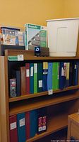 Photo showing wooden shelves holding multiple binders in various colors, boxed business card sheets, envelopes, and the Panasonic electric pencil sharpener.