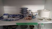 Shelf display showing multiple blue and white porcelain pieces, pedestal bowls, small Delft dish, and white lidded container.