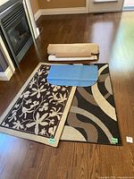 View of two small area rugs partially rolled and laid out on hardwood floor, with multiple underpads including a blue anti-slip pad on one rug, and two rolled beige pads.