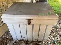 Front view of a white plastic deck box showing lid, latch, and wear marks.