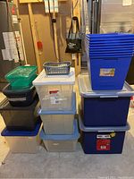 Stack of plastic storage totes and bins in basement setting with various colors and sizes visible