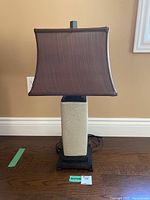 Full view of the ceramic base table lamp showing the textured beige ceramic body, dark wooden base, and the brown square fabric shade.