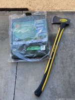 Photo showing the packaged green woven polyethylene tarp along with the Collins axe on concrete ground.