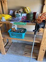 Photo showing assembly of utility items including various rope, spools of twine, packaged hardware, utility grabber tool, and extension cords on wood shelving
