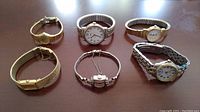 Six vintage ladies watches displayed on a surface showing various bands, dials, and styling.
