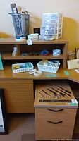 Photo of desk area showing 2-drawer wheeled file cabinet, plastic drawer organizer, scissors, and letter openers arranged on top and side.