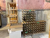 Photo of two wooden wine racks, folding metal rack, and assorted wine bottles in basement setting