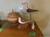 Wood and ceramic decor assortment including two wooden birds, ceramic penguin, and wood container with lid on wooden surface