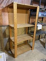 Full view of the wood storage shelf showing three slatted wood shelves and pegboard back panel in basement setting
