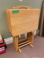 Four wooden folding TV tables stacked vertically on a wooden storage rack. Tag indicates dimensions 19.5 x 10 x 30.5 inches.