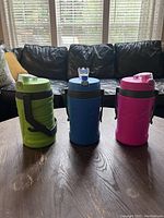 Photo of three Under Armour Sideline water bottles in green, blue, and pink on a wooden surface with a couch in the background.