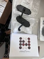 Two dark bronze Ashley Norton Chiltern door handles with curved levers and rectangular backplates resting on protective packaging next to an Ashley Norton branded box.