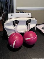 Two red bowling balls with white stripes placed in front of a black and white bowling bag on table.