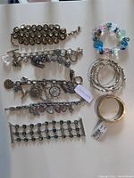 Image showing various bracelets laid out including charm bracelets, beaded bracelet, multiple stone-set bangles and a gold-tone bangle with red design.