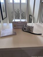 Nikon Coolpix S6000 digital camera front with wrist strap alongside original box and quick start guide manual.
