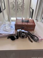 Photo showing Canon PowerShot A620 camera, original box, software CD, manuals, USB cable, wrist strap, and four AA batteries in sealed package.