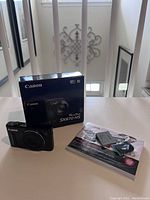 Canon PowerShot SX610 HS camera with original box, battery, USB cable and manuals on table