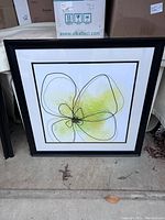 Front view of a framed artwork with a stylized flower in black lines and green-yellow watercolor inside double black frames with white matting.