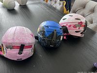 Three child-sized Giro ski helmets with different designs on a table, showing backs and sides.