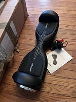 Photo of black Jetson hover board placed on wooden floor with charger and user manual beside it.