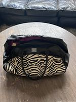 Front and top angle showing black and white zebra print with black handles and purple interior lining inside the open main compartment.