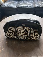 Black and white zebra print Liz Claiborne travel bag on a wooden table with black handles visible, showing the front and side detail of the bag.