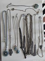 Full view of all 10 long chain necklaces arranged side by side on a flat surface showing pendants and chain details