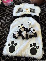 Top view of the white and black panda sleeping bag with five stuffed pandas on it, showing panda face on hood and paw prints.