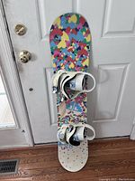 Full view of the colorful heart-designed snowboard with white bindings attached showing overall shape and design.