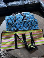 Four Scout storage bags; three blue and brown floral patterned under-the-bed bags stacked, and one multicolor striped storage bag in front.