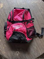 Front view of the bright pink Speedo backpack showing large front pocket with Speedo logo, side mesh pockets, and multiple zipper compartments.