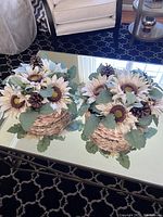 Photo of two round woven white baskets with artificial sunflower centerpieces placed on glass table in living room.
