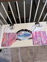 Three Turtle Fur neck warmers laid out on a white table, showing their multi-colored striped and tie-dye patterns.