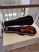 Violin placed inside open black hard case showing violin body, bow, and resin box.