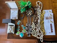 Overview of all jewelry including necklaces, bracelets, earrings, watch box, nail polish strips, and green mesh pouch with additional pieces.