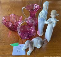 Wide view of all cranberry glass pieces and all three Lladro figurines on wood surface.