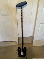 Full view of black carbon fibre curling broom standing upright with the pair of black Gold Line shoes below it.
