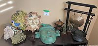 Wide view of assorted decorative items including statues, plaques, a mask, oriental urn, figurines, a tea kettle, and a gong