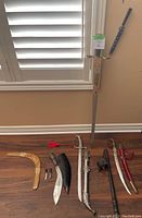 Various decorative items arranged on a floor including a wooden boomerang, knives with sheaths, a spiked mace, a large decorative sword with sheath, and a smaller curved sword with red tassel.