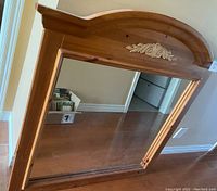 Framed mirror with arched wooden frame featuring a carved floral motif at the top.