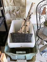 Photo of plastic storage bins stacked with birch poles and a dark woven rectangular basket inside the white bin.
