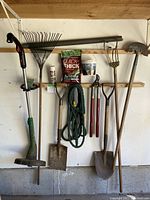 Photo showing a hanging display of garden tools including weed eater, rake, shovels, cultivator, edger, loppers, garden hose, and gardening supplies such as grass seed and plant starter