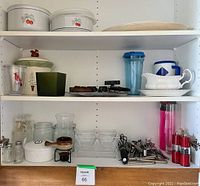 Shelving with ceramic serving dishes, cookie jars, glass pitchers, plastic travel mugs, and kitchen utensils.