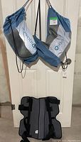 Pair of VQ Orthocare catalyst propel knee braces hanging by their drawstring bags on a white door in a basement setting