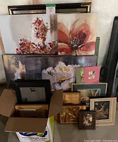 Overview of the lot showing multiple framed paintings with floral themes, wooden frames, and boxed smaller frames and photo album