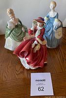 Three Royal Doulton female figurines in various historic dresses photographed on wooden floor.